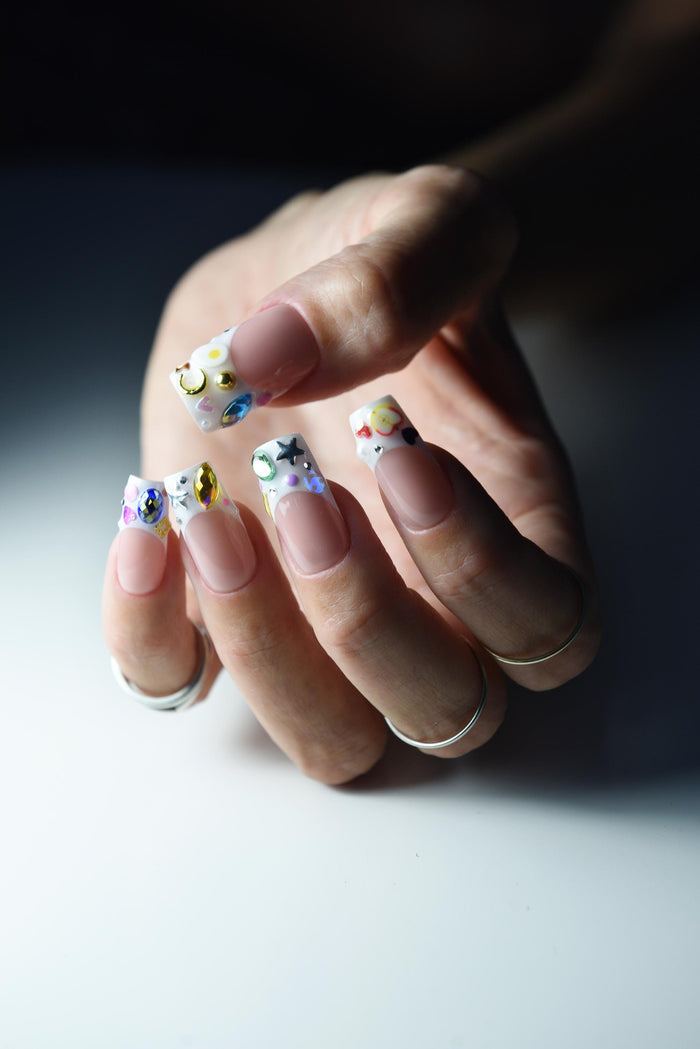 Nude pink French press-on nails with colourful gems and painted tip details – detail view