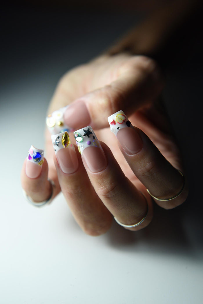 Nude pink French press-on nails with colourful gems and painted tip details – detail view