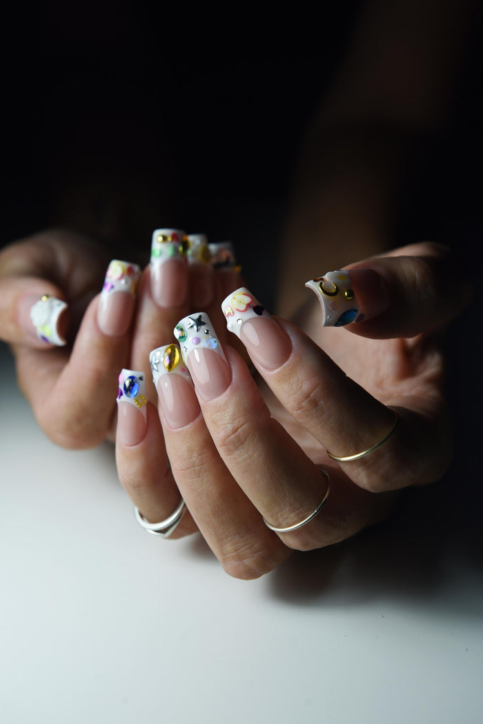 Nude pink French press-on nails with colourful gems and painted tip details – detail view
