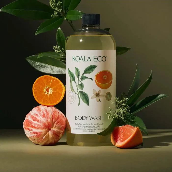 A bottle of body wash on a dark olive surface with citrus fruits and green leaves arranged around it.