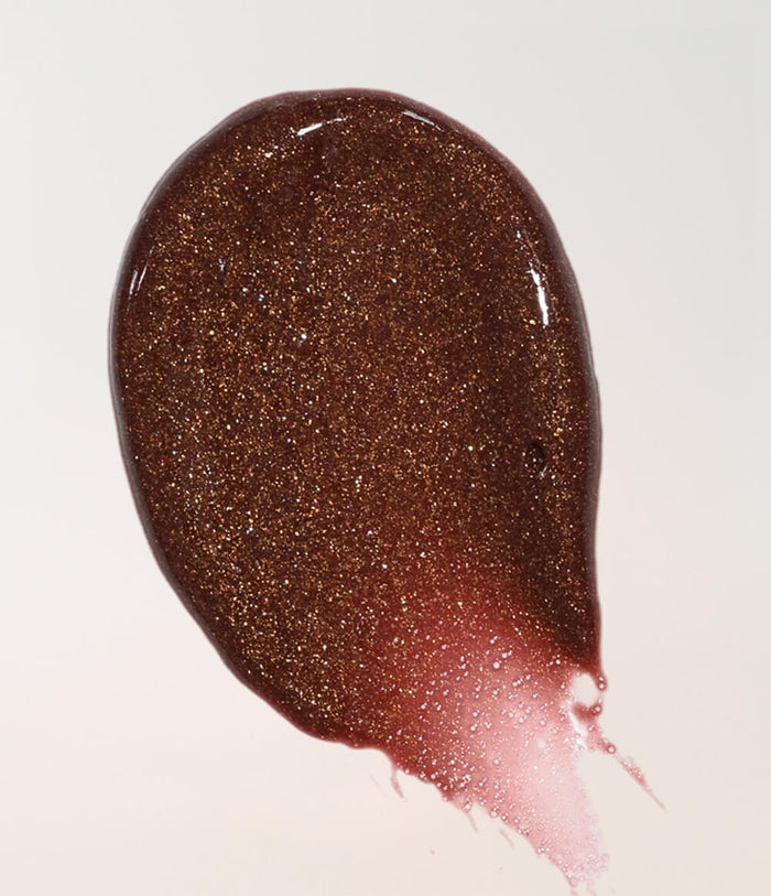 A glossy, textured smear of dark brown glitter lip gloss or gel on a clean white background, showing fine shimmer and a subtle pinkish tint near the bottom edge.