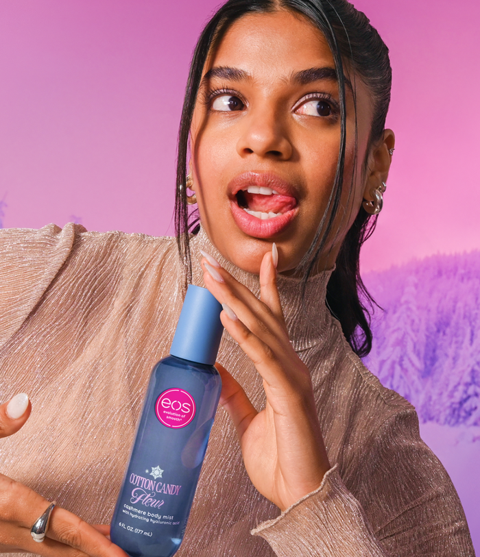 A woman holding a bottle of EOS Cotton Candy against a pink and purple background.
