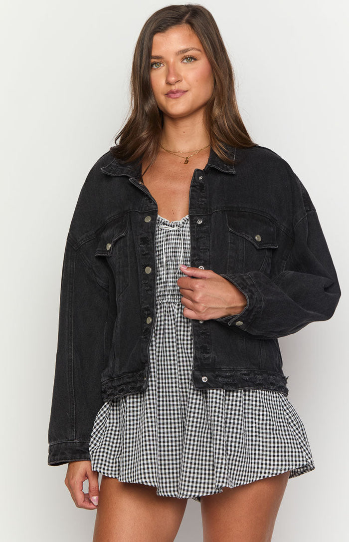 Front view of a black washed oversized denim jacket with a collared neckline, button-front, and distressed hem