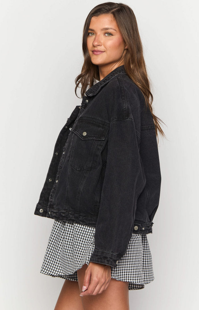 Side view of a black oversized denim jacket with a distressed raw hem and silver button details