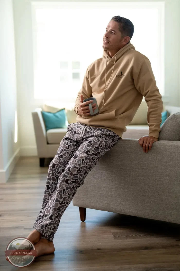 Local Boy Outfitters L1600022 Men's Joggers in Localflage Camo lifestyle image of man wearing them leaning on couch enjoying coffee