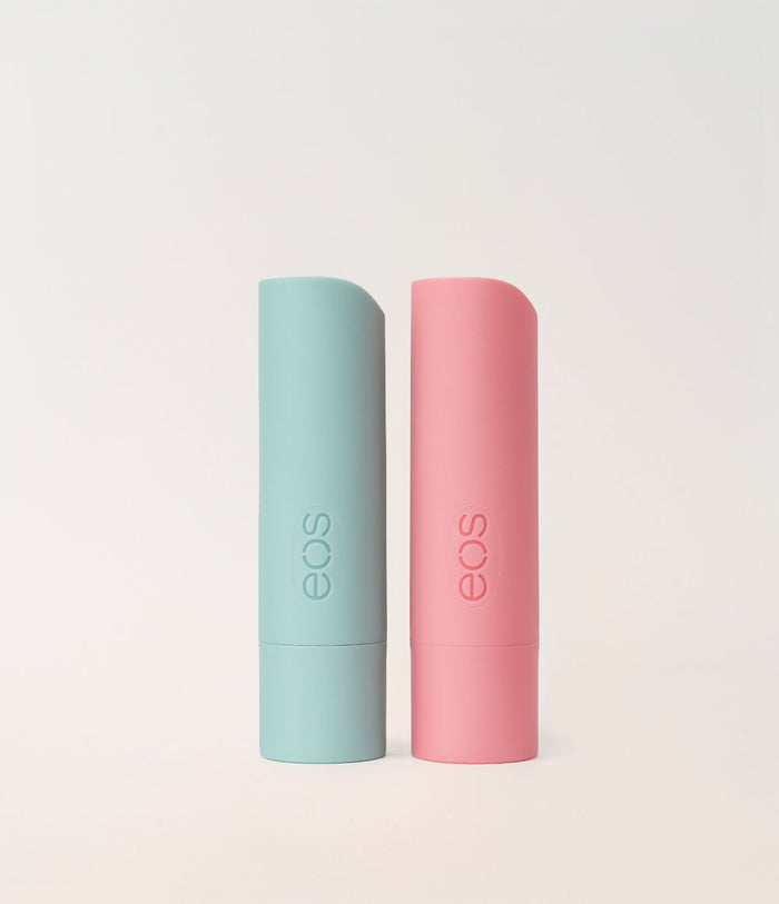Two EOS lip balm tubes standing upright on a light beige background, one in mint green and one in soft pink.