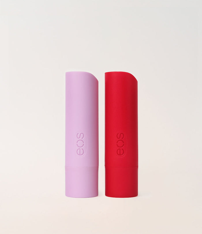 Two EOS lip balm tubes standing upright on a clean off-white background, one in light lavender and one in bright red.