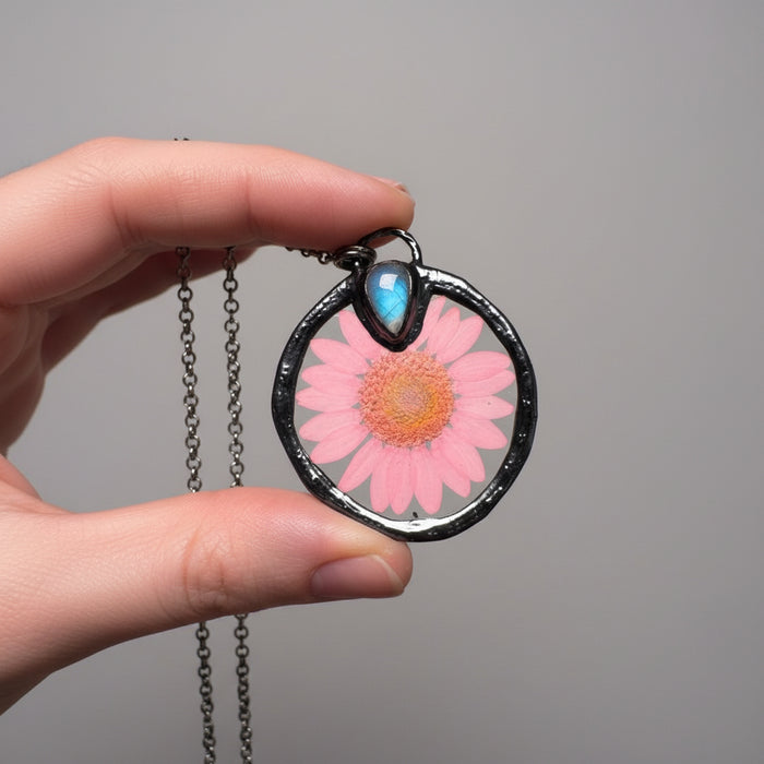 Necklace with a pink flower pendant held by a hand