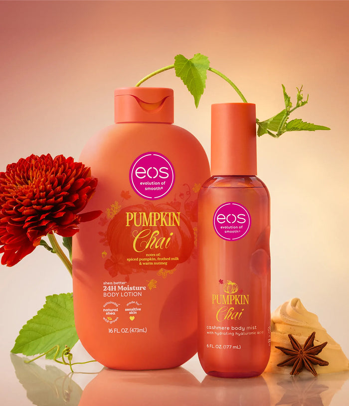 Two EOS Pumpkin Chai moisturizing body care products, a large pump bottle and a smaller spray bottle, styled with a red flower, green leaves, and star anise against a warm peach gradient background.