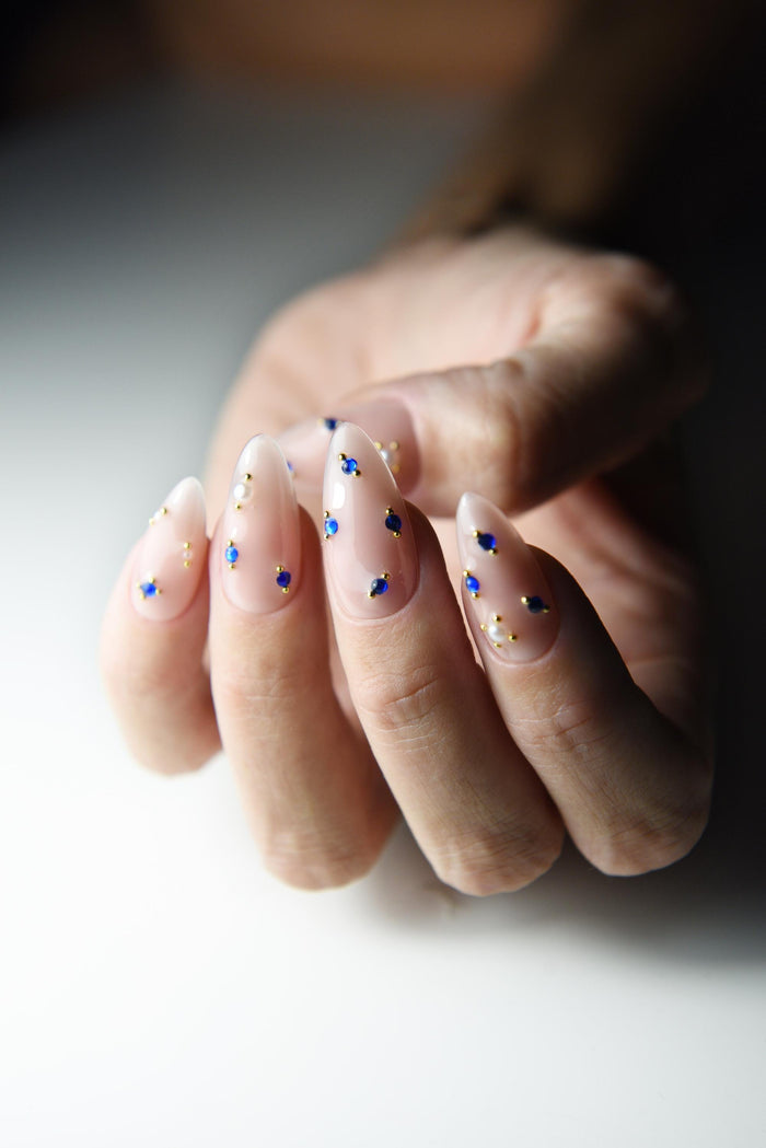 Milky nude press-on nails with sapphire blue crystals and gold accents – detail view