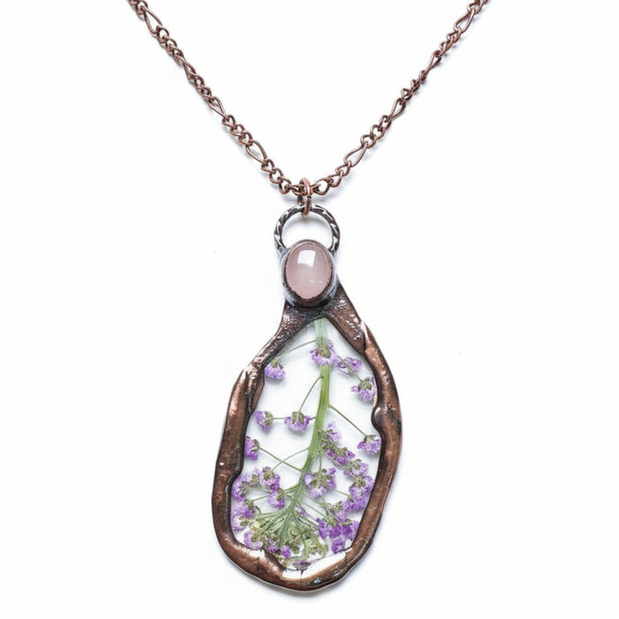 Teardrop-shaped pendant with pressed flowers and a rose quartz stone on a white background
