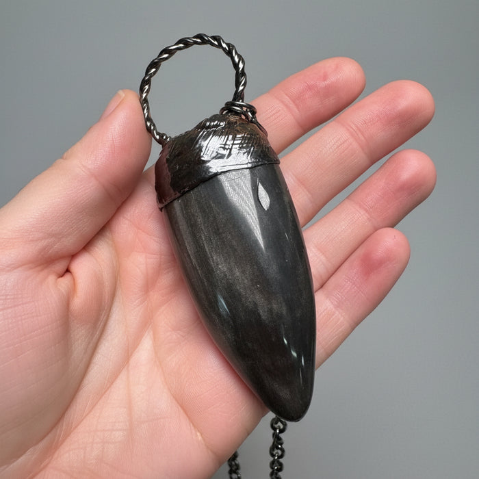 Hand holding a dark stone pendant with a chain against a gray background
