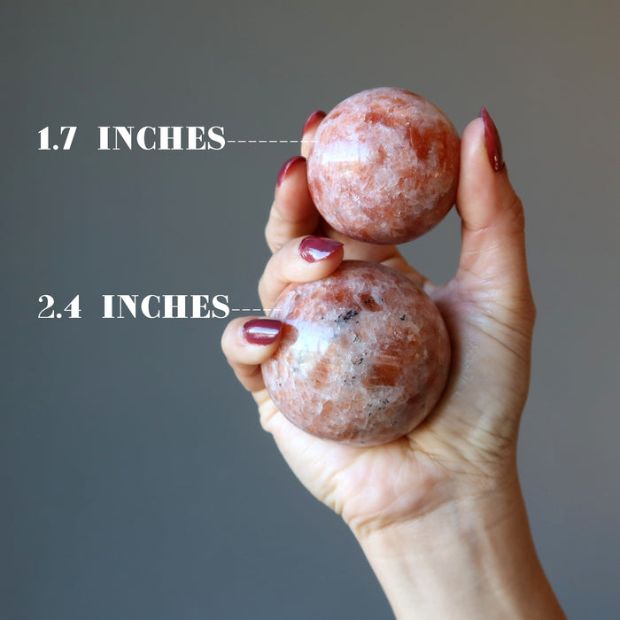 hand holding two sunstone spheres to show size difference