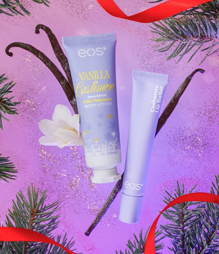 Two EOS cosmetics tubes, Vanilla Calmurn body lotion and Gashmere Lip Butter, arranged on a purple glitter background with pine branches, vanilla beans, a white flower, and red ribbon.